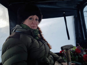 A short winter's tale about remote living with Linda Mellor in thick winter clothing sitting in Argocat holding valentines day flowers and a shovel